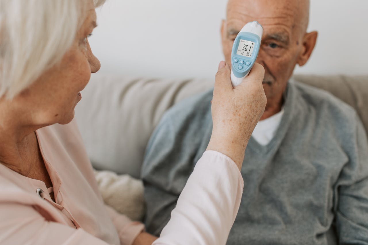 Home An elderly woman checks the temperature of a senior man using a digital thermometer indoors.