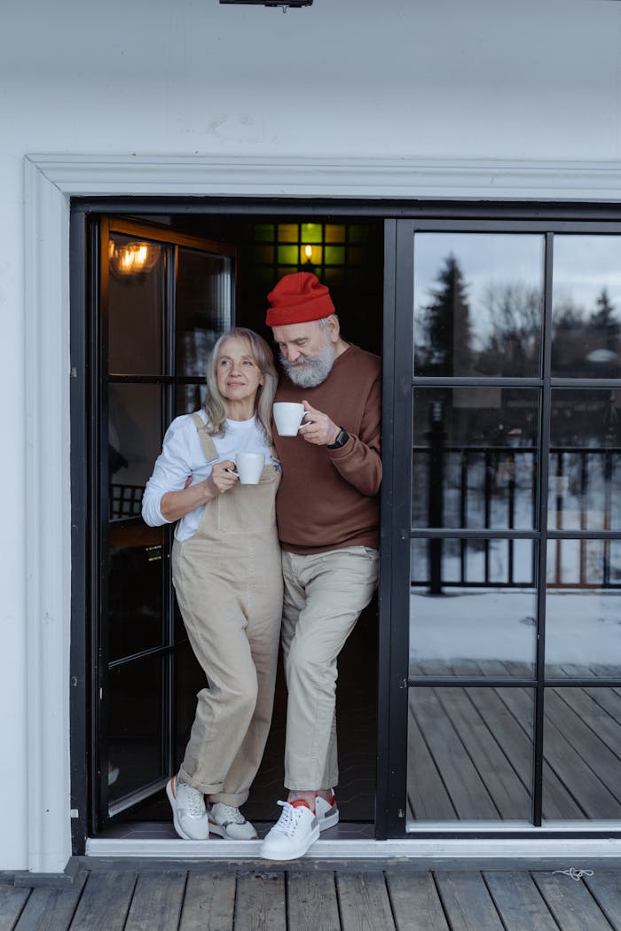 Home Elderly couple sipping coffee at home by the balcony during winter.